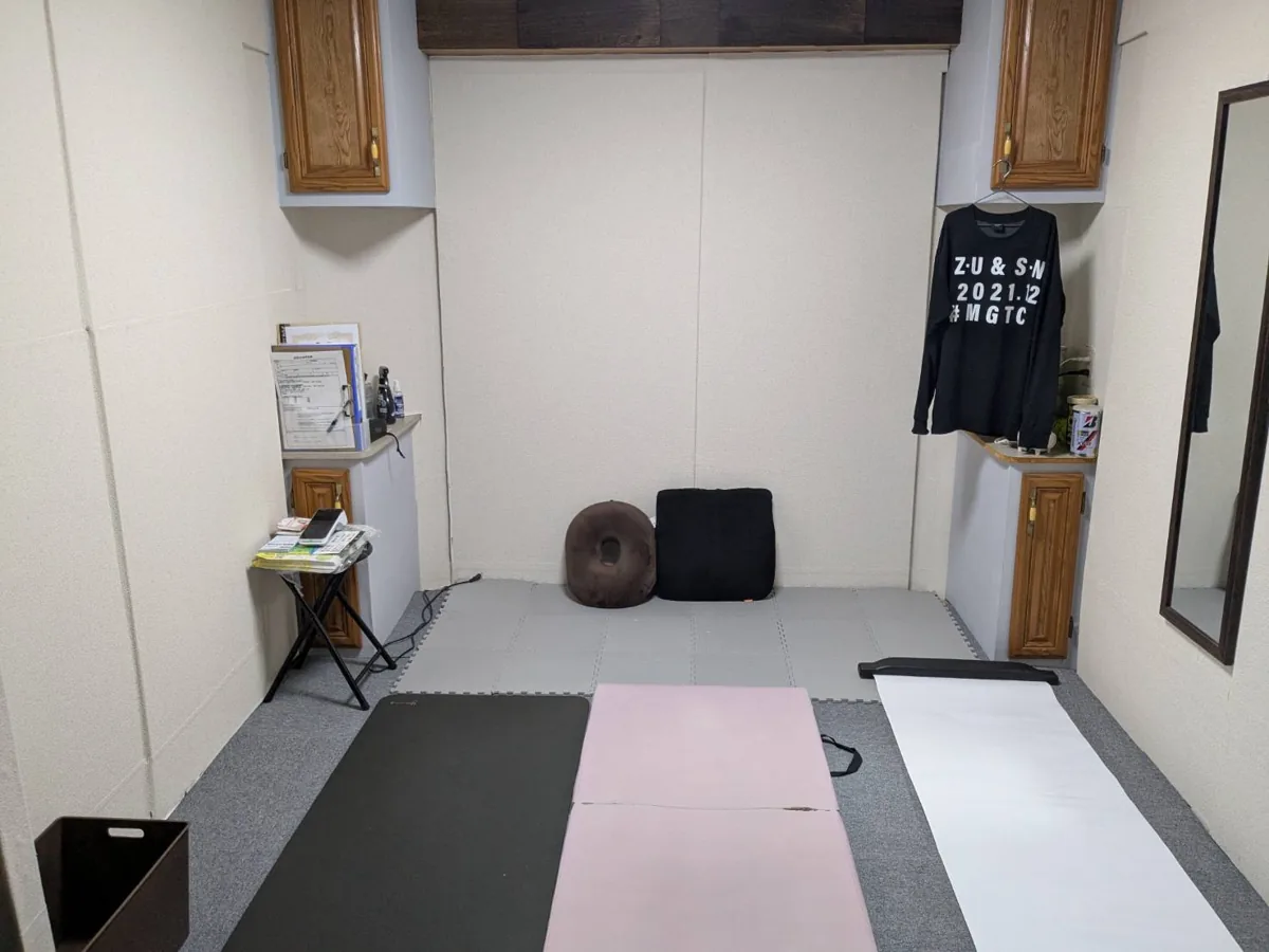 スタジオの内観。マットを敷いたトレーニングスペースと鏡、クッション